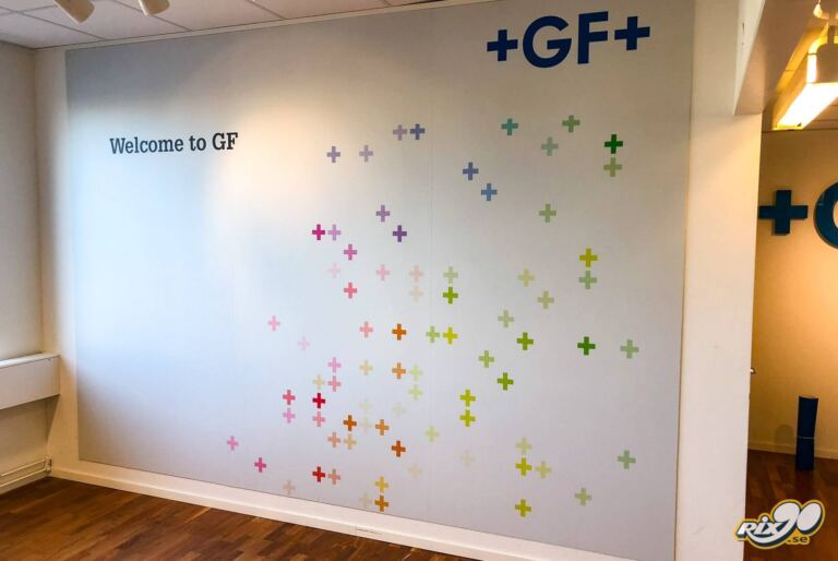 Väggdekor med färgade kors och texten Welcome to GF i kontorsentré