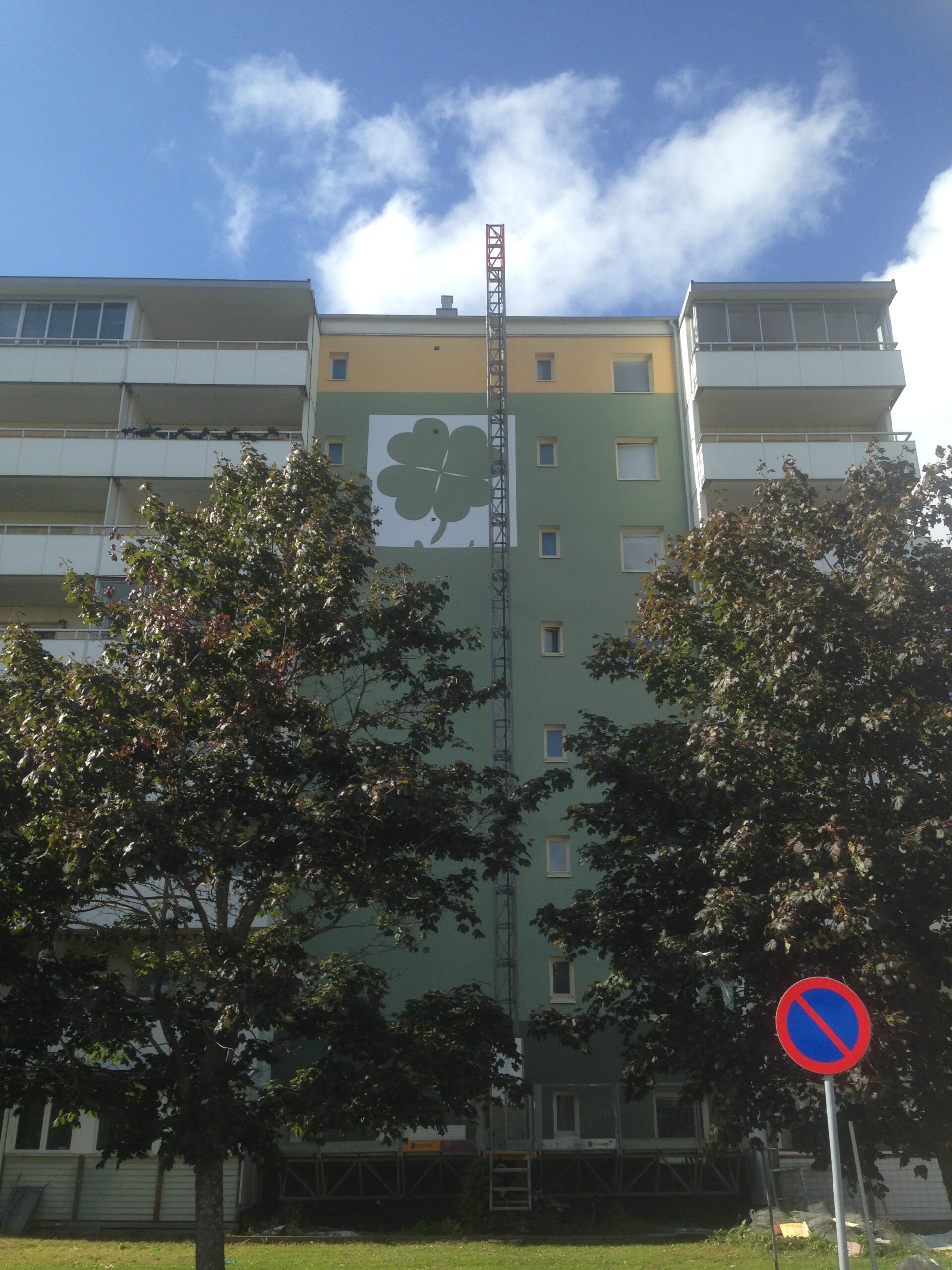 Schablon för fasadmålning Stor schablon uppsatt på flerbostadshusets fasad för målning av fyrklöver, monterad från hisslift på nionde våningen