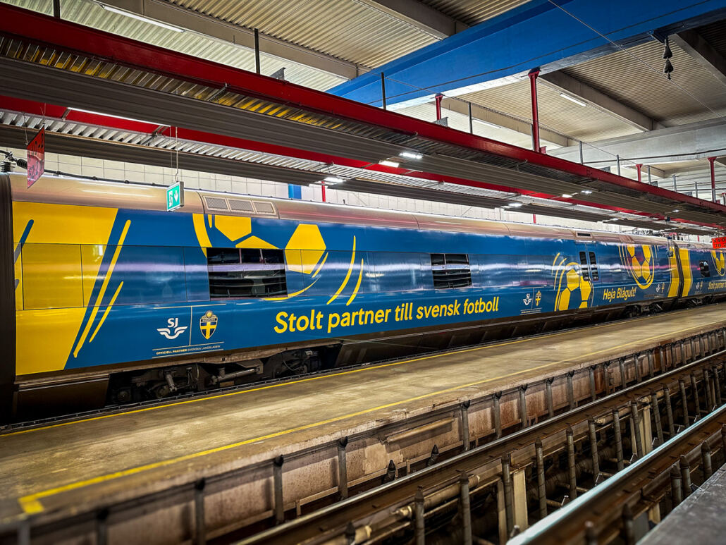 Helfolierad SJ-vagn i blått och gult med fotbollsmotiv och texten Stolt partner till svensk fotboll Helfolierad SJ-vagn i blått och gult med fotbollsmotiv och texten Stolt partner till svensk fotboll