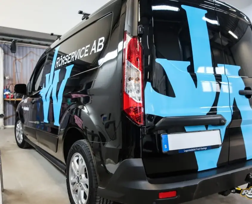 Stora ljusblå bokstäver i reflekterande folie på svart Ford Transit Connect till rörserviceföretag